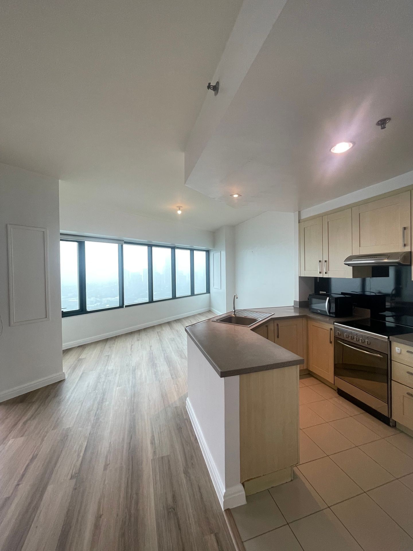 Interior view of a modern apartment with large windows, showcasing a kitchen island and wooden flooring.