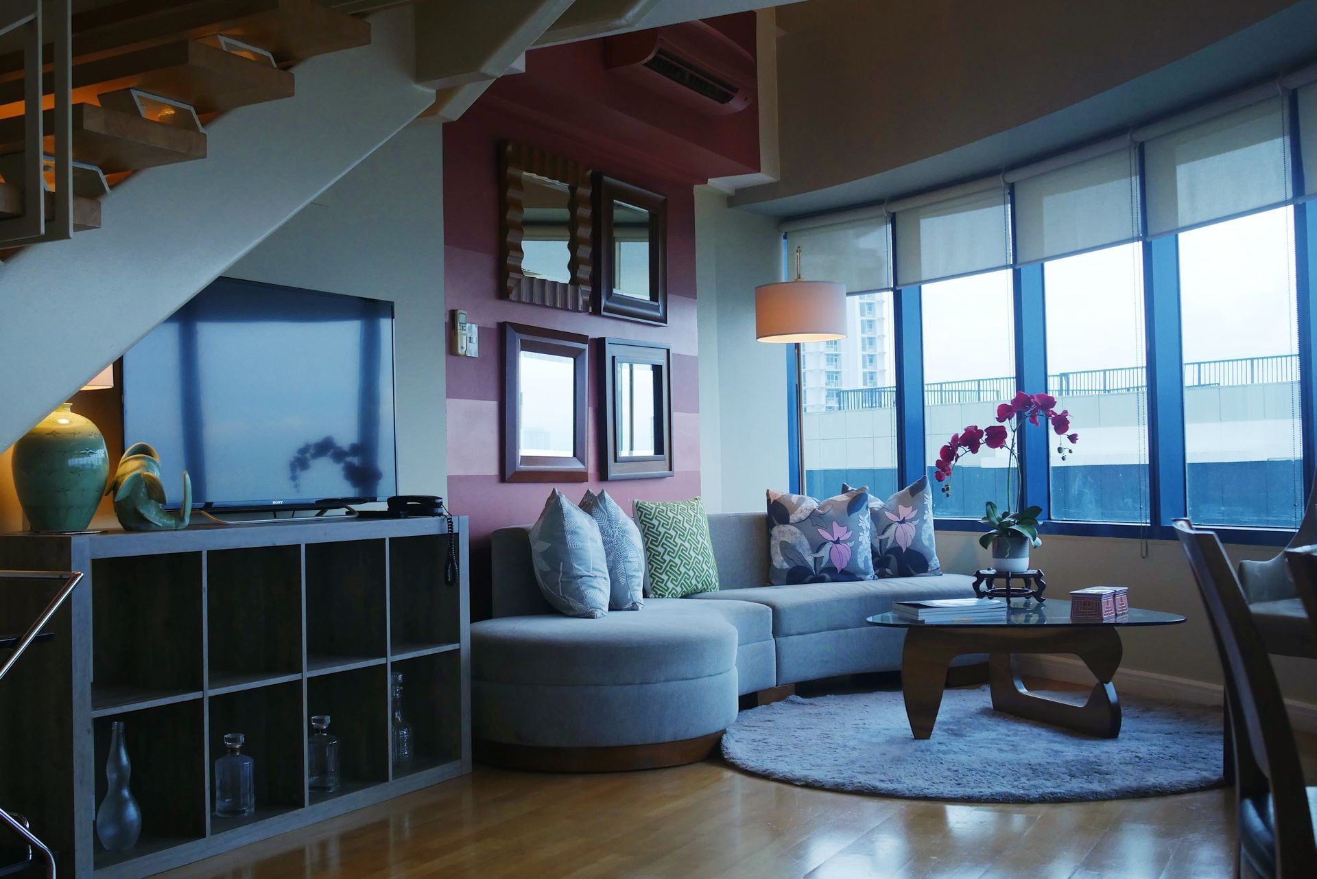 Modern living room with a grey sectional sofa, TV, decorative pillows, and large windows.